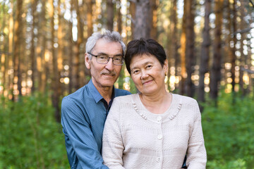 Fototapeta premium portrait of a happy loving 60s old couple outdoors in a park. elderly Asian man and woman in a limp on the background of trees. the concept of a happy retirement