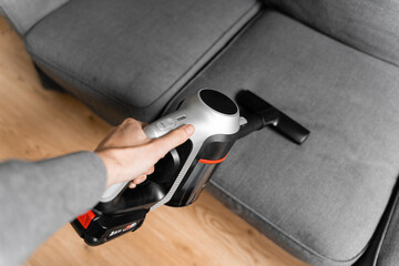 Cleaning grey sofa with wireless vacuum cleaner. Handheld cordless cleaner. Household appliance....