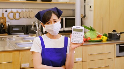 電卓を持ちやりくりに悩むマスクをした家事代行の女性作業員