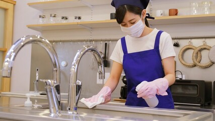 キッチンを清掃して除菌する家事代行のマスクをした女性作業員