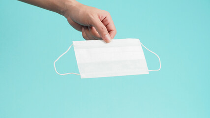Hand is holding White surgical face mask or disposable mask on mint green or Tiffany Blue...