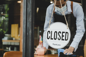 Closed. sign board hanging on glass door and waitress staff wearing protection face mask cleaning...