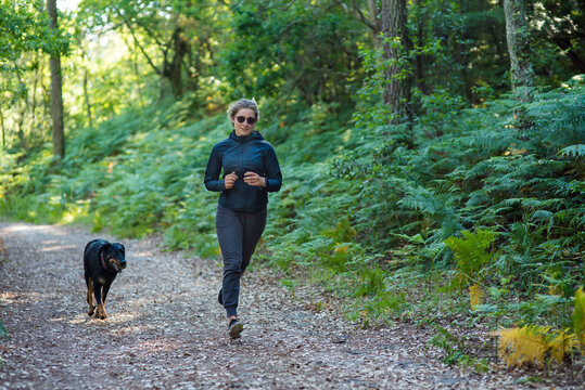 beautiful young woman jogging with her dog in the forest