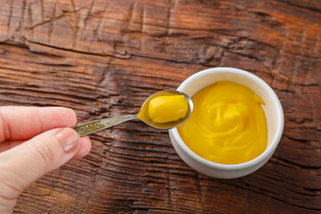 Sauce boats with cheese sauce and hand with sauce in a spoon on a wooden table.