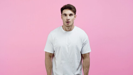 Amazed man in white t-shirt looking at camera isolated on pink
