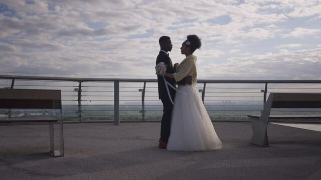 Slow dance of happy confident African American couple of newlyweds on romantic summer bridge outdoors. Bride and groom in wedding suit and dress dancing first dance. Romance and love