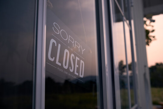 Sorry we are closed sign board through the glass of coffee shop or restaurant .