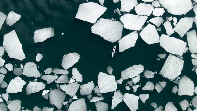 Kayak sailing between ice floes on Baikal lake in spring. Aerial drone view. Baikal lake, Siberia, Russia