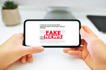 Online fake news on a mobile phone. Woman holding a smartphone with fake news in front of the monitor with fake news. Propaganda, misinformation. Horizontal photo.