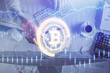Double exposure of man's hands typing over computer keyboard and crypto currency theme hologram...