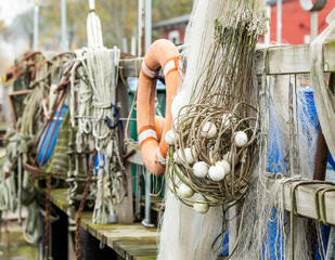 A selection of fishing equipment hanging on wooden railings. In focus are a trawl, a gillnet, and a lifebuoy.