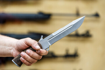 A large army knife in the hand of a buyer on the background of a shop window. Sale of edged weapons...