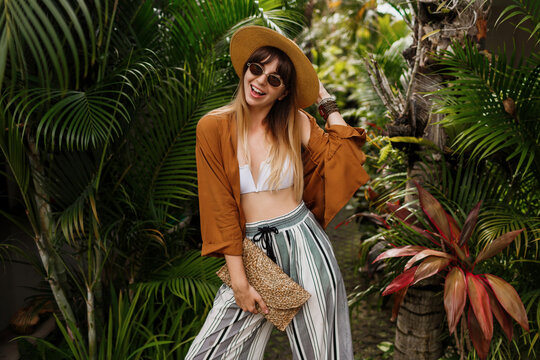Fashion  image of  sexy graceful  woman in straw hat posing on tropical palm leaves background in Bali. Wearing stylish bohemian accessories.