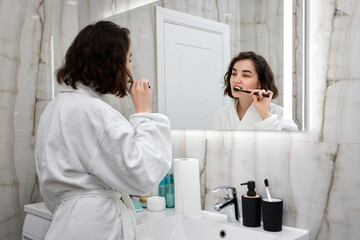woman in white bathrobes brushing teeth in front of mirror