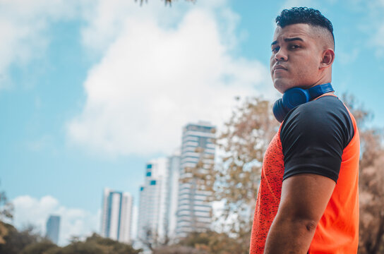 athletic man of Latino origin after training with a tough attitude with a yellow sweater or walks with a hood and a bad man's face, Venezuelan model in the park with buildings in the background