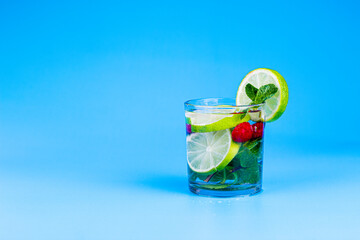 Cocktail in glass with lemon, lime, mint and raspberries on aqua blue background.