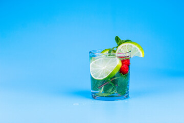 Cocktail in glass with lemon, lime, mint and raspberries on aqua blue background.