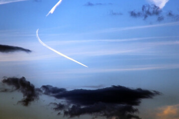 Natural landscape background. Evening sunset sky with clouds with white stripes from passed by air plane