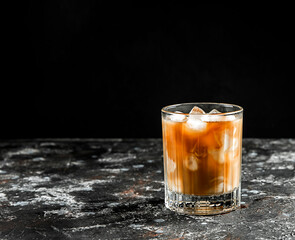 Cold coffee with ice and cream in a glass on a dark background.