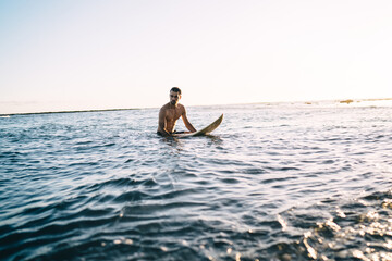 Athletic young man with surfboard relaxing in ocean water
