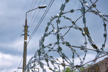 Barbed wire on a fence against a cloudy sky.