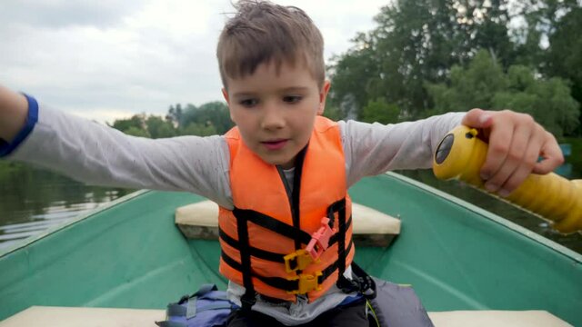 Boy rowing boat children. Kid float on a boat river city holiday. Kid rides a boat with paddle. Child rowing oars on a boat a lake park city. Recreation children's camp during holidays on the river