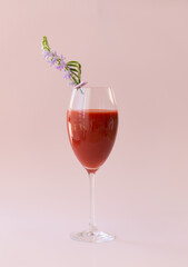 A beautiful glass with a strawberry and banana smoothie, decorated with flowers on a light pink background.
