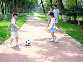 Happy family of four playing football in the park
