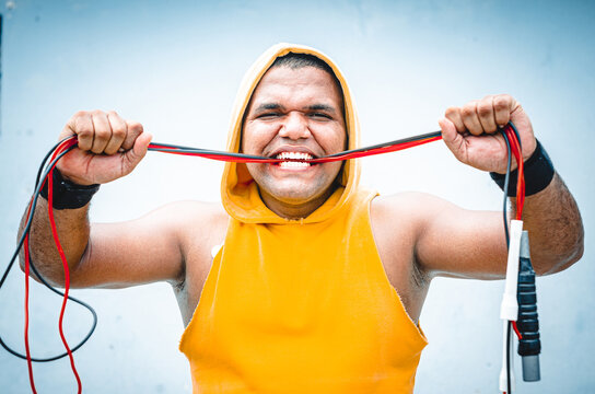 athletic man of Latino origin after training with a tough attitude with a yellow sweater or walks with a hood and a bad man's face, Dominican model in sport biting the jump rope