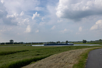 Twentekanaal and river IJssel intersection in flat Dutch landscape near Zutphen with a large cargo ship passing by against a  blue sky with cumulus clouds above
