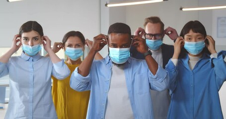 Multicultural businesspeople wearing safety mask standing in office - Powered by Adobe