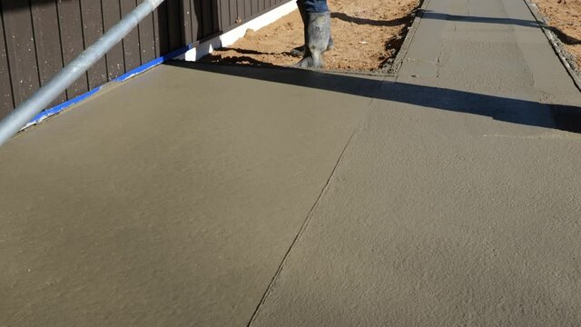 Concrete bull float is used on new cement concrete by a worker to bring liquid to the surface and to level, and smooth the new sidewalk at a New Home Construction job site.