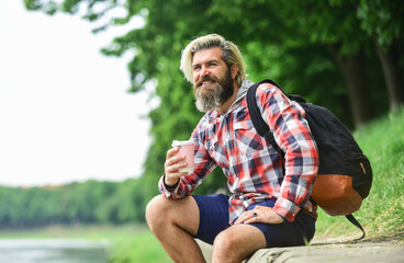 Naklejka na ściany i meble Handsome calm bearded man outdoors with a cup of coffee. Man drinking hot coffee. tourist relaxing in park drink tea or coffee. Coffee on the go. man with a cup outdoors