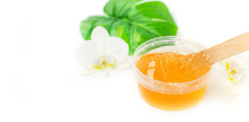 Sugar paste or wax honey in a transparent jar and white orchid on a white background. Sugaring. Depilation and beauty concept. Waxing.
