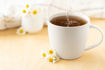 Chamomile tea with kitchen towel and chamomile in white ceramic cup on the wooden table. Herbal tea. Side view