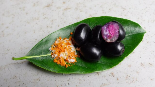 Spicy mixed salt with some black java plum fruit in the green leaves. A way to eat ripe cesium camini fruit by hand. 4k closeup video.