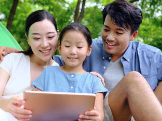 Happy family of three uses tablet computer outdoors