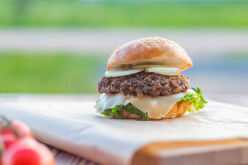 Small depth of field. Soft focus. Burger made it at home. Next to it are red tomatoes on a branch. Close-up.