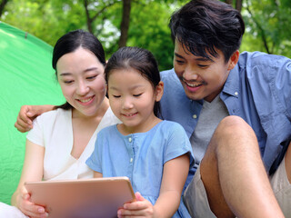 Happy family of three uses tablet computer outdoors