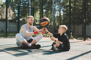 Professional basketball player instructor putting ball on finger of little sportive kid boy sitting...