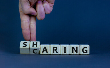 Sharing is caring symbol. Businessman turns wooden cubes and changes the word 'sharing' to 'caring'. Beautiful grey table, grey background. Business, sharing is caring concept. Copy space.