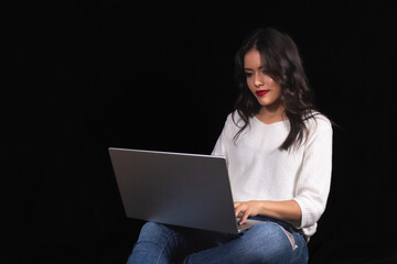 Naklejka premium Beautiful young girl sitting using laptop, on black background.