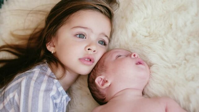 The older sister takes care of the newborn brother. Two young children are lying on the bed. The concept of love and childcare.