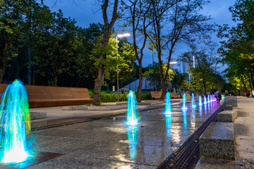 Colorful sparkling water from fountain on touristic promenade in Kolobrzeg, Poland during spring evening at the baltic sea. - obrazy, fototapety, plakaty