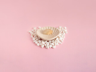 A seashell with pearl rock surrounded by white little rocks, on a pale pink background