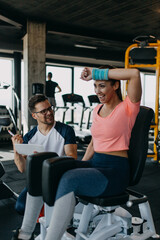 Fototapeta na wymiar Young fit and attractive woman working out in modern gym together with her personal fitness instructor or coach.
