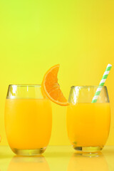 two glasses with orange juice, half an orange next to the glass on the yellow background