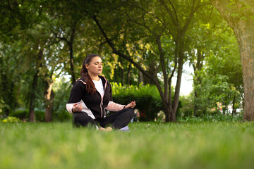 beautiful girl meditates in the lotus position on the green grass surrounded by trees. yoga class in nature