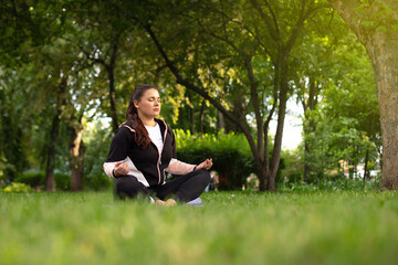 beautiful girl meditates in the lotus position on the green grass surrounded by trees. yoga class...