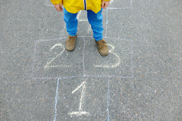 Little boy's legs and hopscotch drawn on asphalt. Child playing hopscotch game on playground on spring day. Outdoors activities for children.